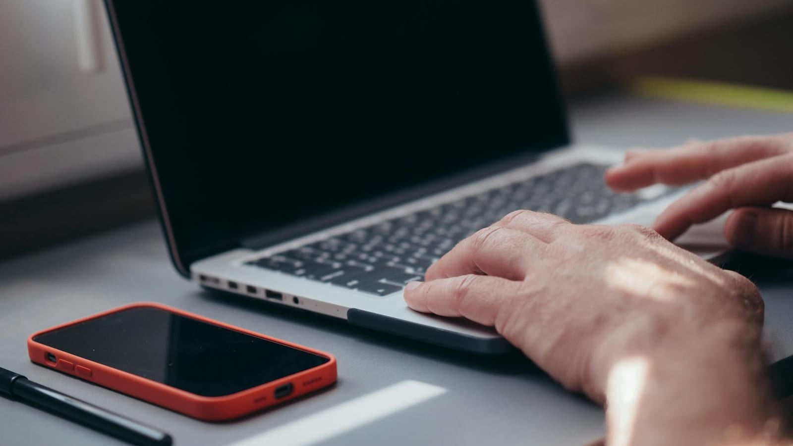 Hands typing on a laptop beside a phone, illustrating JJM Networks IT news and insights from Carlisle, Cumbria